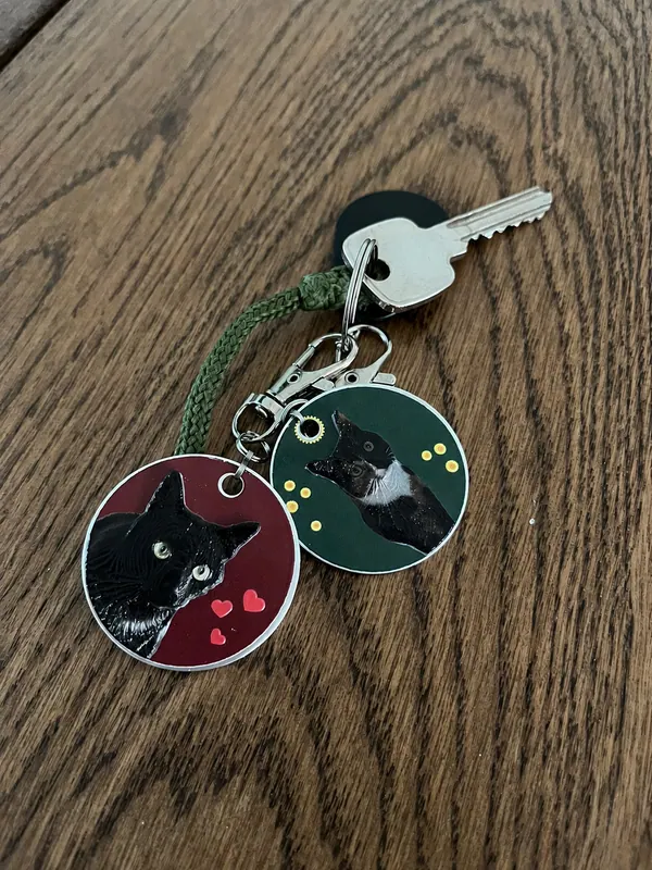 Twee ronde sleutelhangers met foto van een zwarte kat, aan een sleutelbos